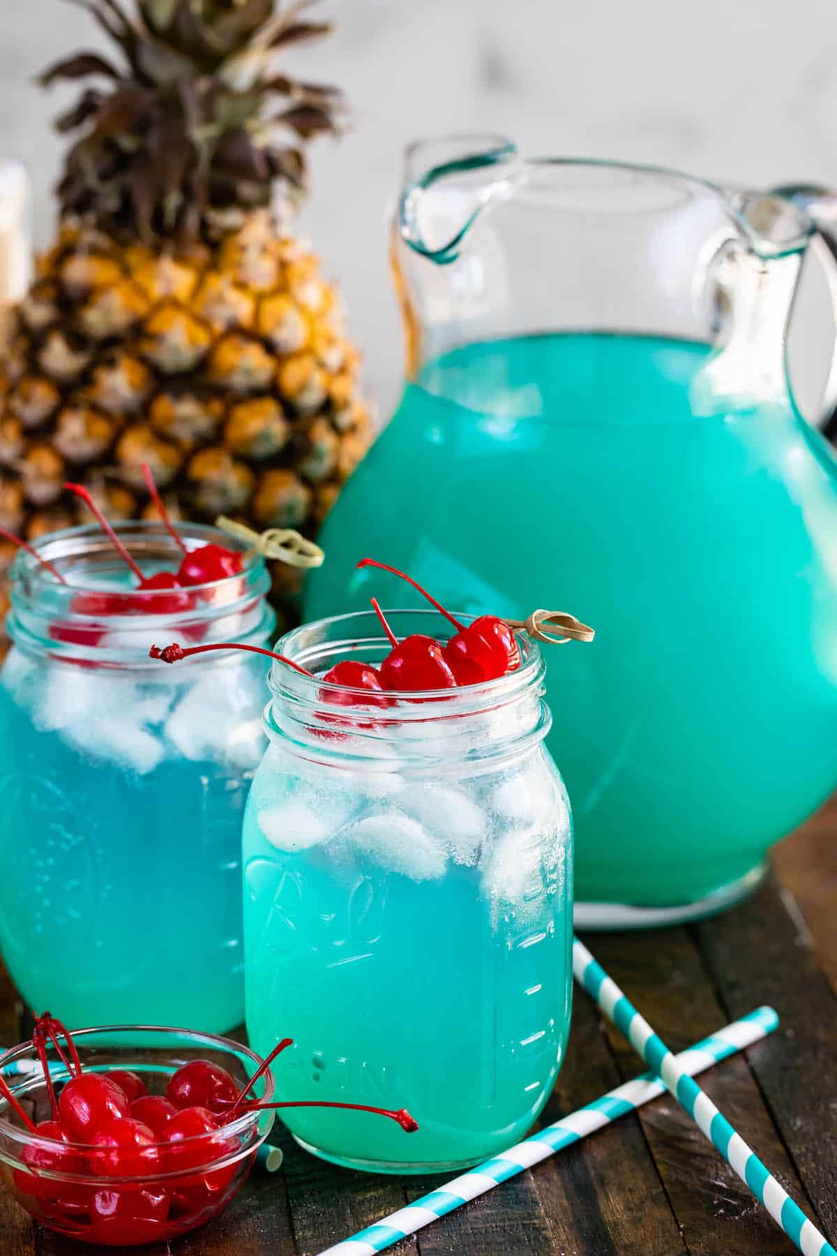 jars of blue drink with 3 cherries and pitcher.