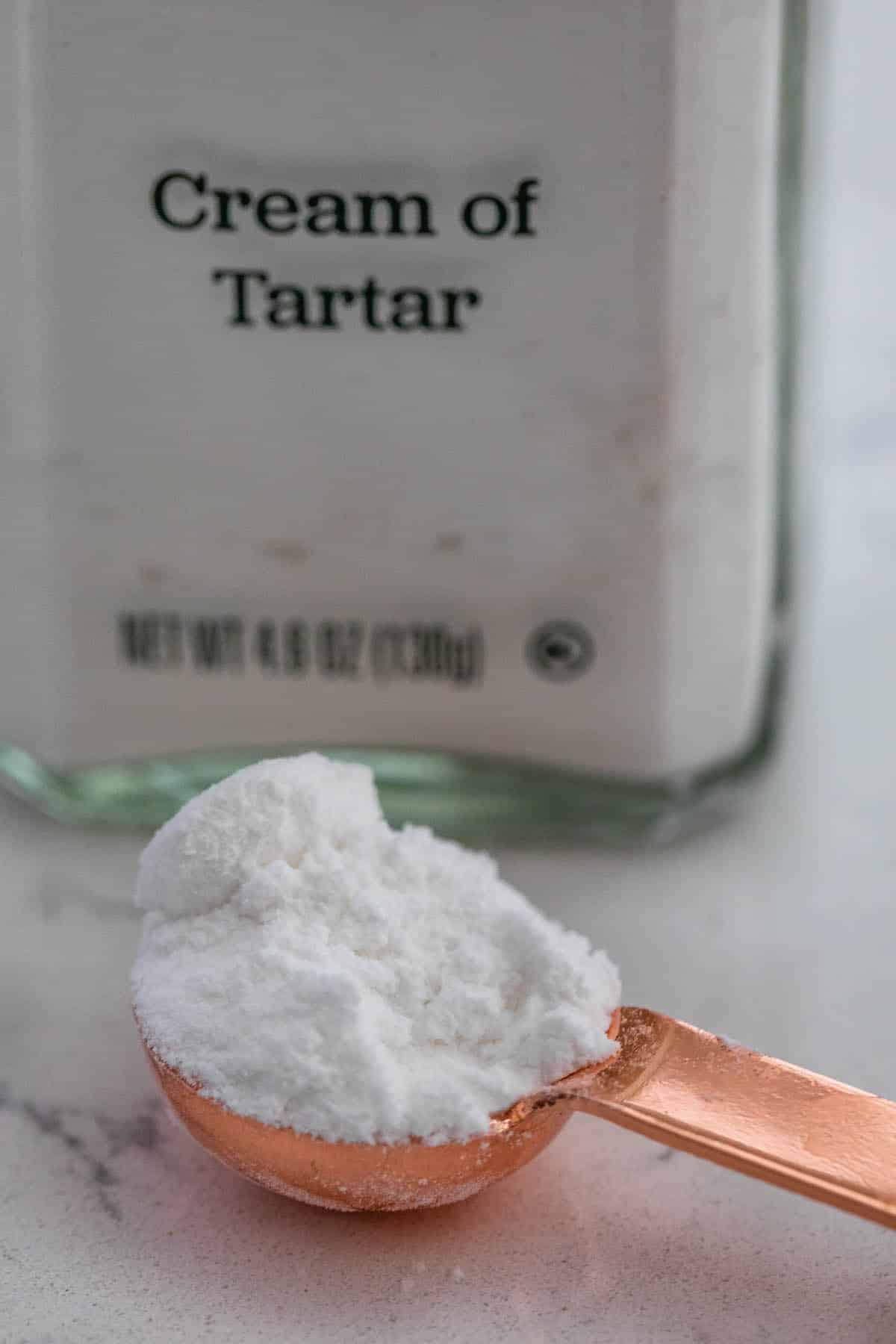 jar of cream of tartar with measuring spoon of it.