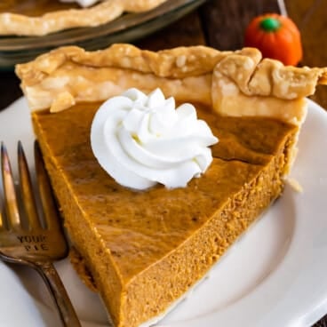 slice of pumpkin pie on white plate with whipped cream and fork
