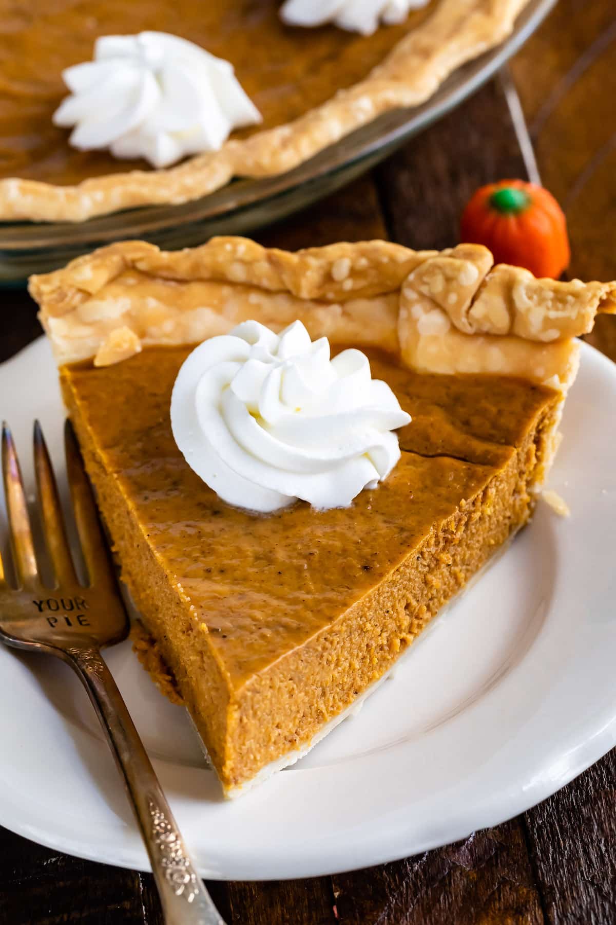 slice of pumpkin pie on white plate with whipped cream and fork