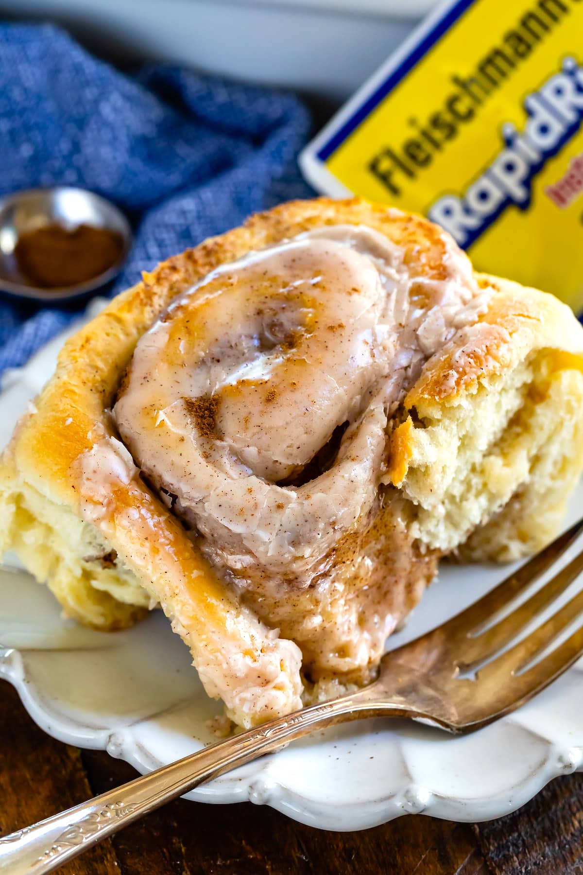 cinnamon roll on white plate with blue napkin behind and fork