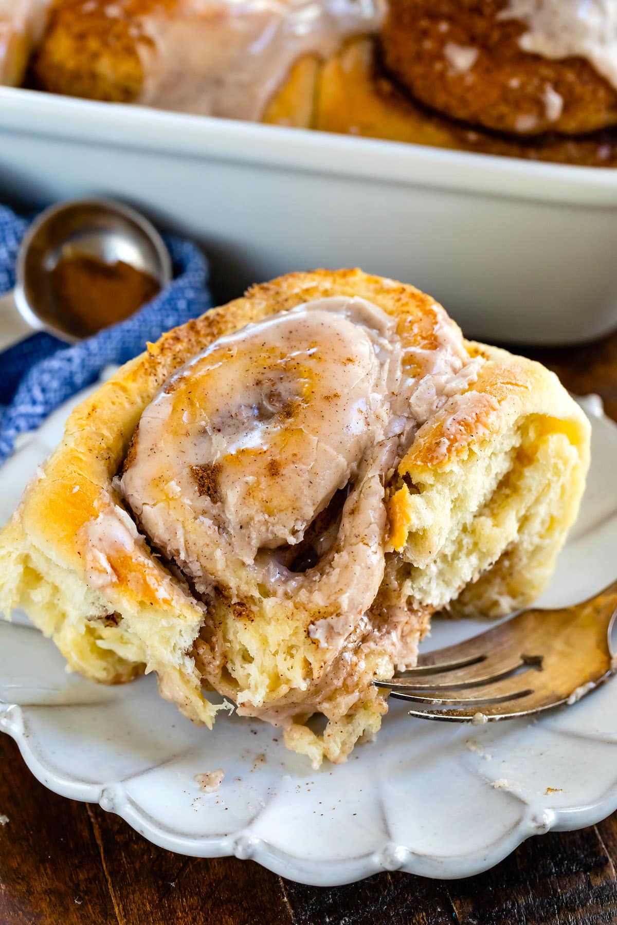 cinnamon roll on white plate with blue napkin behind and fork