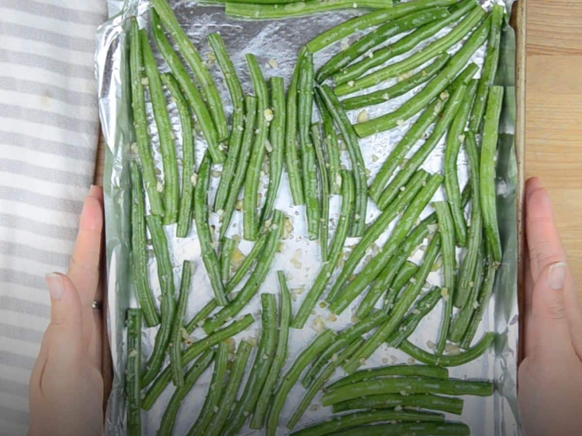 green beans on foil lined cookie sheet with hands on each side.