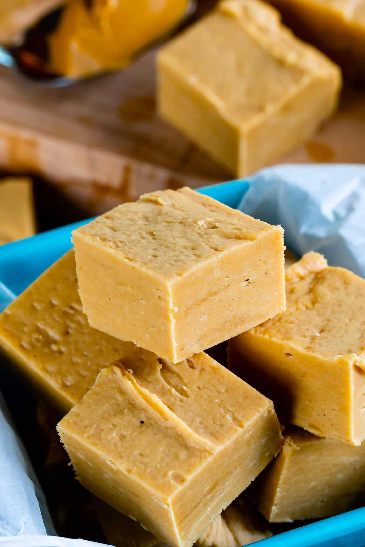 pile of fudge squares in teal container with fudge behind