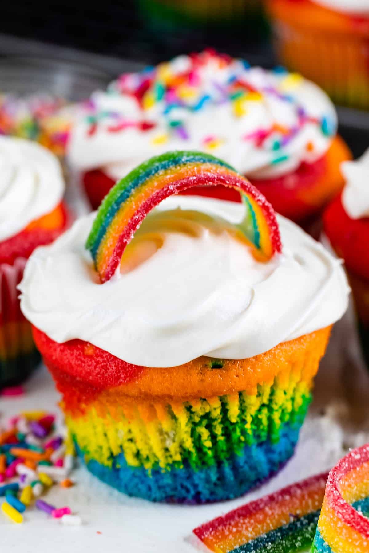 rainbow cupcake with white frosting and rainbow fruit rope on top.