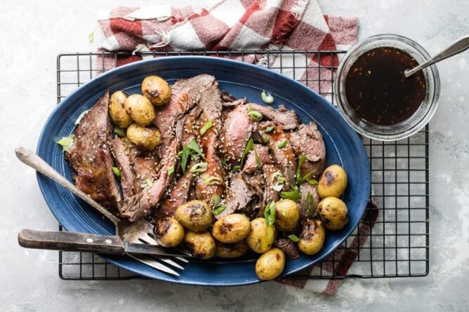 overhead shot of meat and potatoes on blue platter on rack with sauce on side