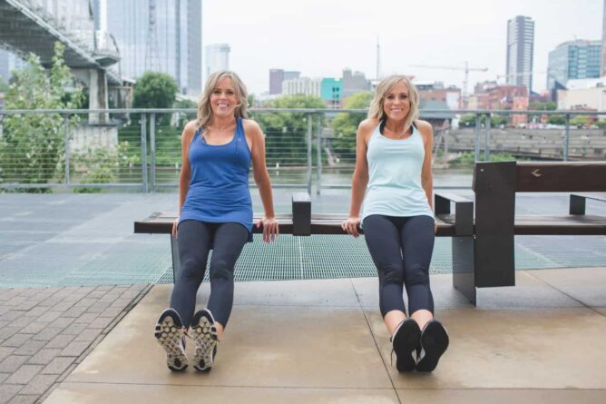 two women exercising on bench with city in the background