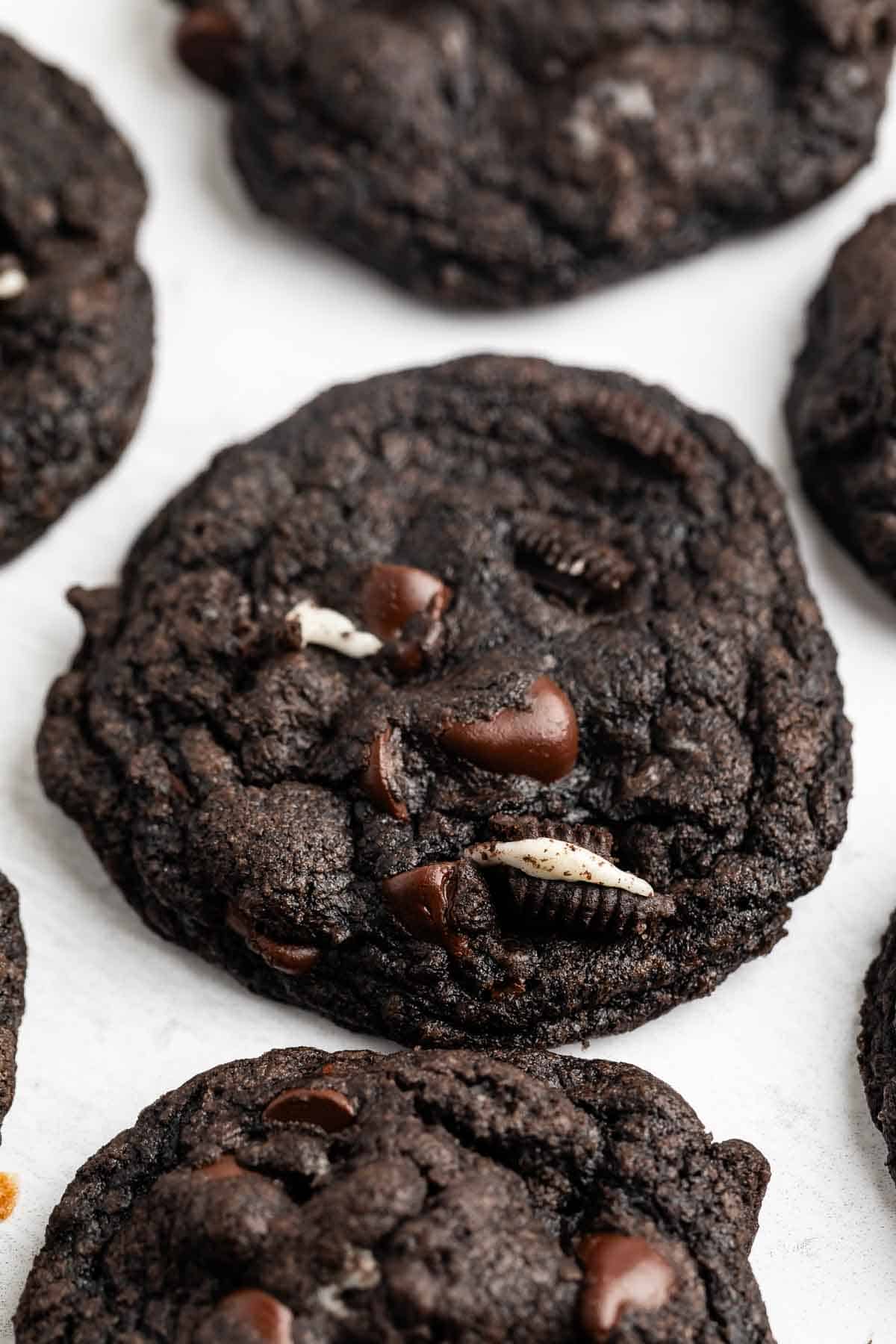 A close-up of Chocolate Oreo Cookies studded with chocolate chips and pieces of cookies and cream on a white surface.