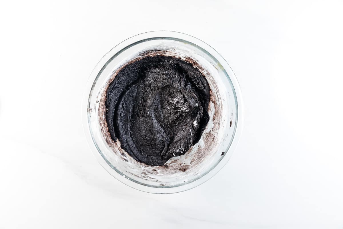 A glass bowl filled with thick, dark chocolate brownie batter sits on a white surface, viewed from above—perfect for creating rich brownies or swirling in chunks of Chocolate Oreo Cookies for extra decadence.