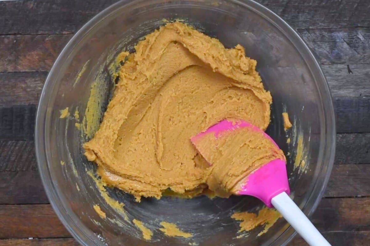 cookie dough in clear bowl on wood table with spatula.