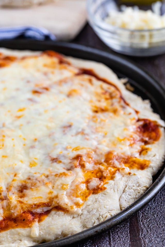 cheese pizza in pizza pan on table with cheese behind