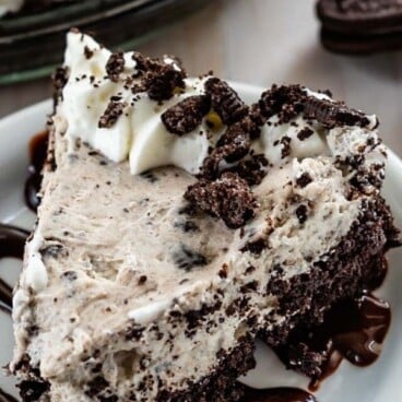 slice of oreo cheesecake on white plate with hot fudge