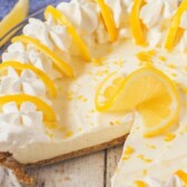 Overhead shot of no bake lemon pie in glass pie dish with one piece missing and recipe title on top of photo in white text