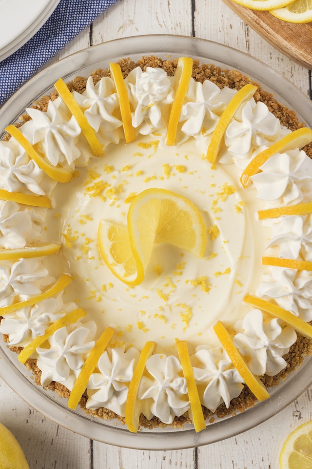 Overhead shot of no bake lemon pie with lemons around it on a white wood table