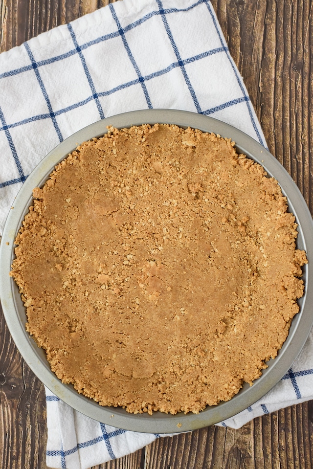 Overhead shot of nutter butter pie crust in dish on wood table with white and blue check napkin