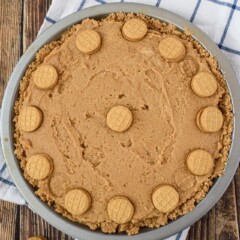Overhead shot of nutella peanut butter pie with nutter butter mini cookies on white and blue checkered napkin on wood table
