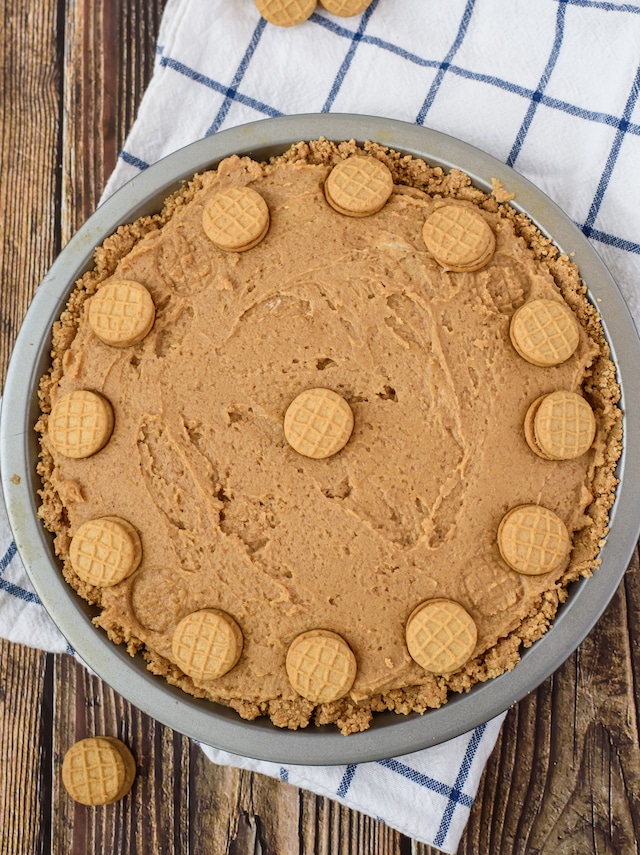 Overhead shot of nutella peanut butter pie with nutter butter mini cookies on white and blue checkered napkin on wood table