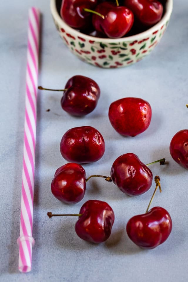 Cherries, a straw and bowl of cherries sitting on counter