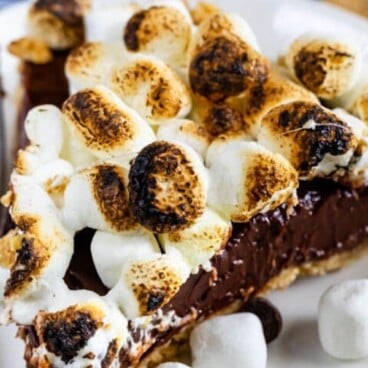 Close up shot of S'mores pie slice on white plate with mini marshmallows and recipe title in text on image