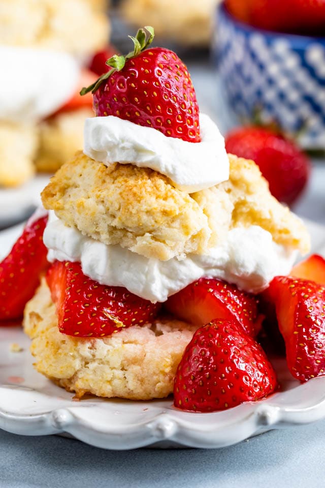 Biscuit strawberry shortcake on white plate with lots of berries and whipped cream