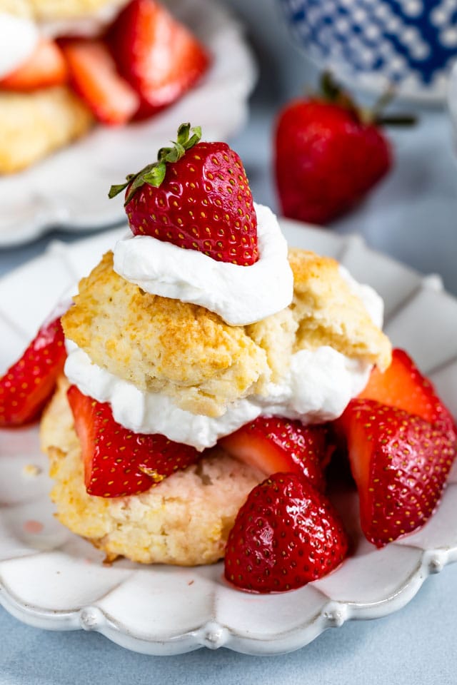 Biscuit strawberry shortcake on white plate with lots of berries and whipped cream