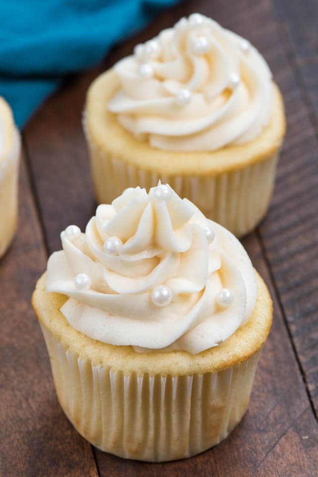 Two vanilla cupcakes with vanilla buttercream frosting on wood table