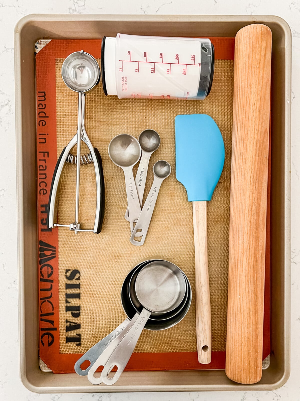 overhead shot of cookie sheet with silpat, cookie scoop, measuring cups, measuring spoons, rolling pin