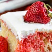 Strawberry jello poke cake slice on white plate with strawberry on top and recipe title on top of image