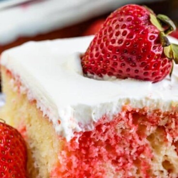 Strawberry jello poke cake slice on white plate with strawberry on top and recipe title on top of image