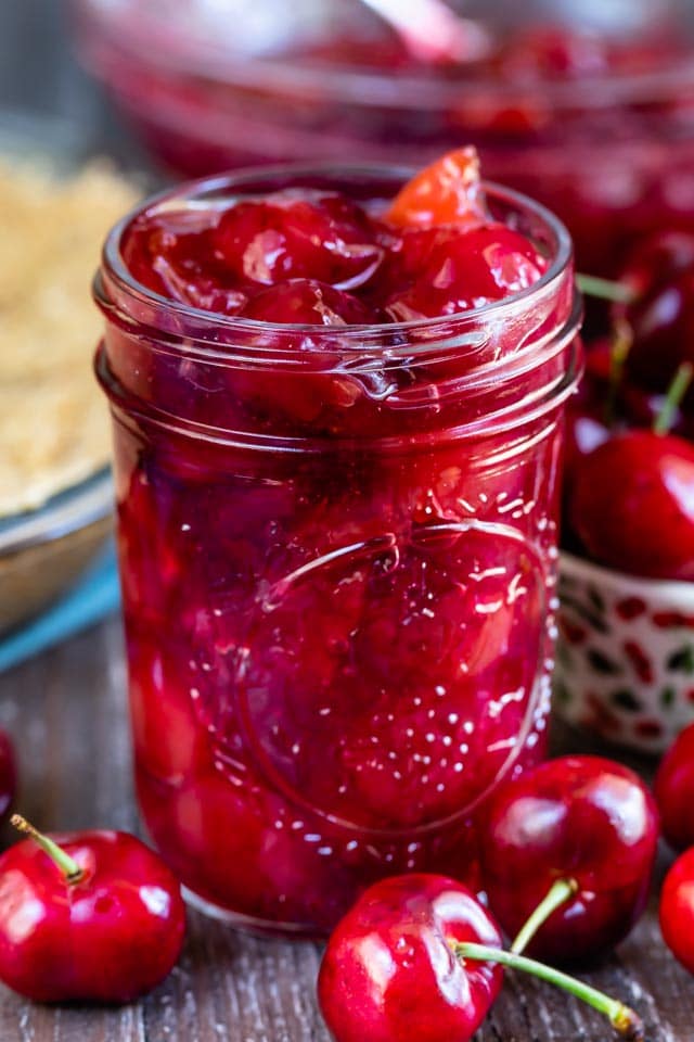Mason jar filled with cherry pie filling with cherries on the table