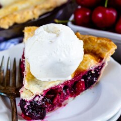 Slice of cherry pie with a scoop of ice cream on top on a white plate with fork