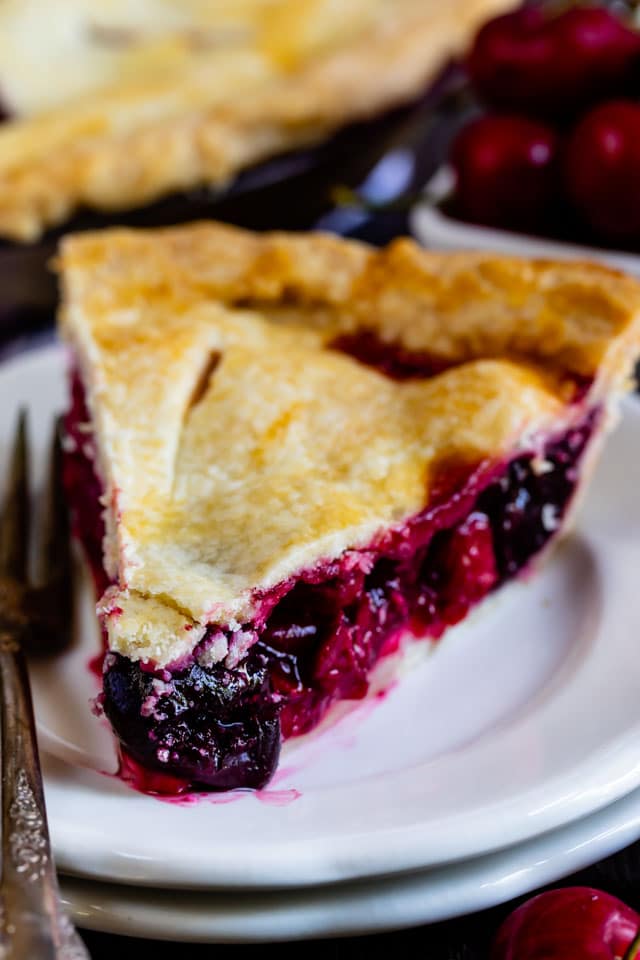 Closeup shot of slice of cherry pie on white plates with silver fork
