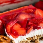 One square of strawberry pretzel salad on a white plate with recipe title in text on top of image