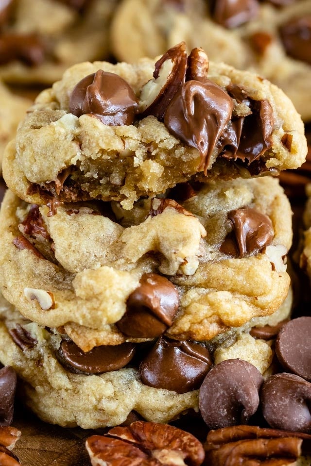 Close up of chocolate chip pecan cookies with one cut in half to show gooey chocolate chips on the inside
