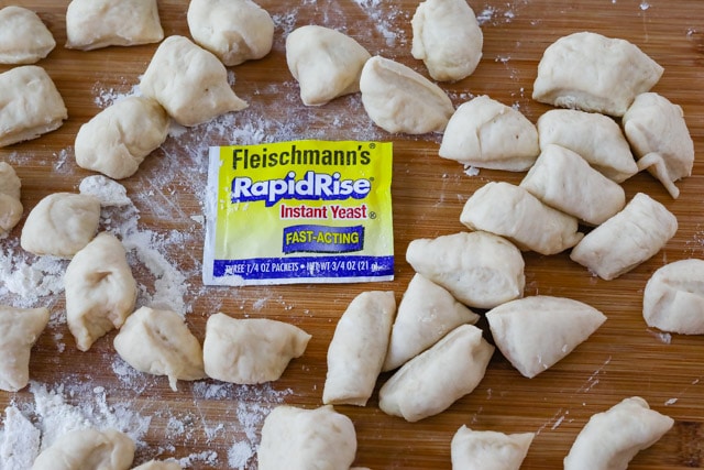 Roll dough pieces on a wood cutting board with yeast packet