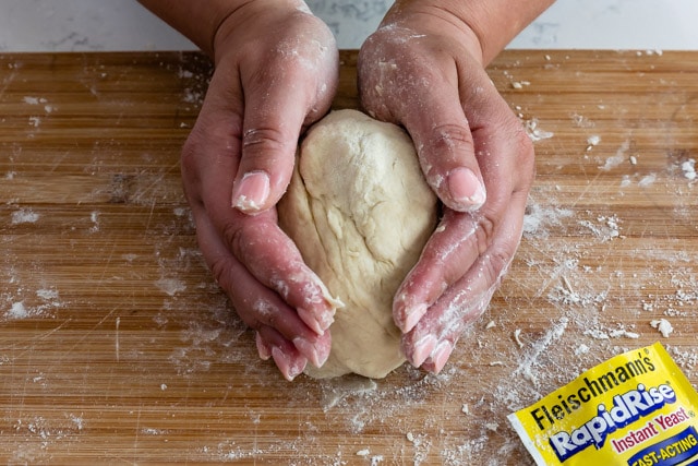 Kneading dough on a wood cutting board with a packet of yeast close by