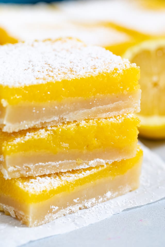 Stack of three lemon bars on a paper towel with lemon wedge in background