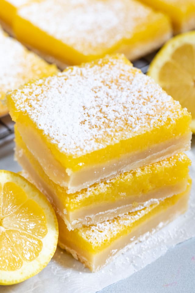 Overhead shot of stacked lemon bars with lemon wedges and powdered sugar on top