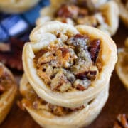 Close up shot of mini pecan pies stacked on top of eachother on cutting board