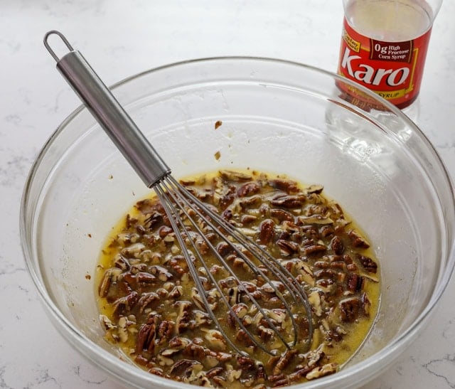 Pecan pie filling in a clear mixing bowl with whisk and karo corn syrup in background