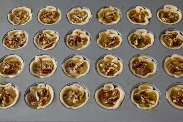 Overhead shot of mini pecan pies in a muffin tin before baking