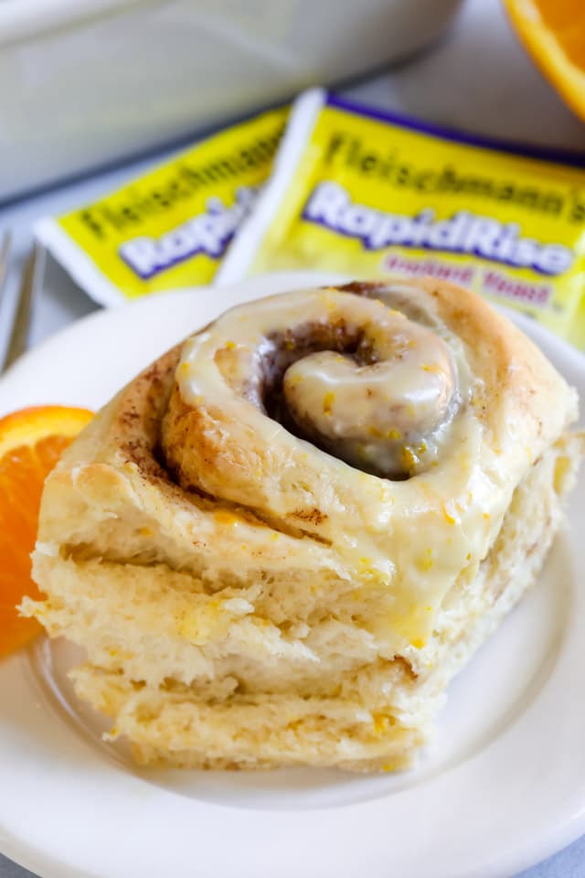 Close up of an orange sweet roll on a white plate with yeast packets behind it
