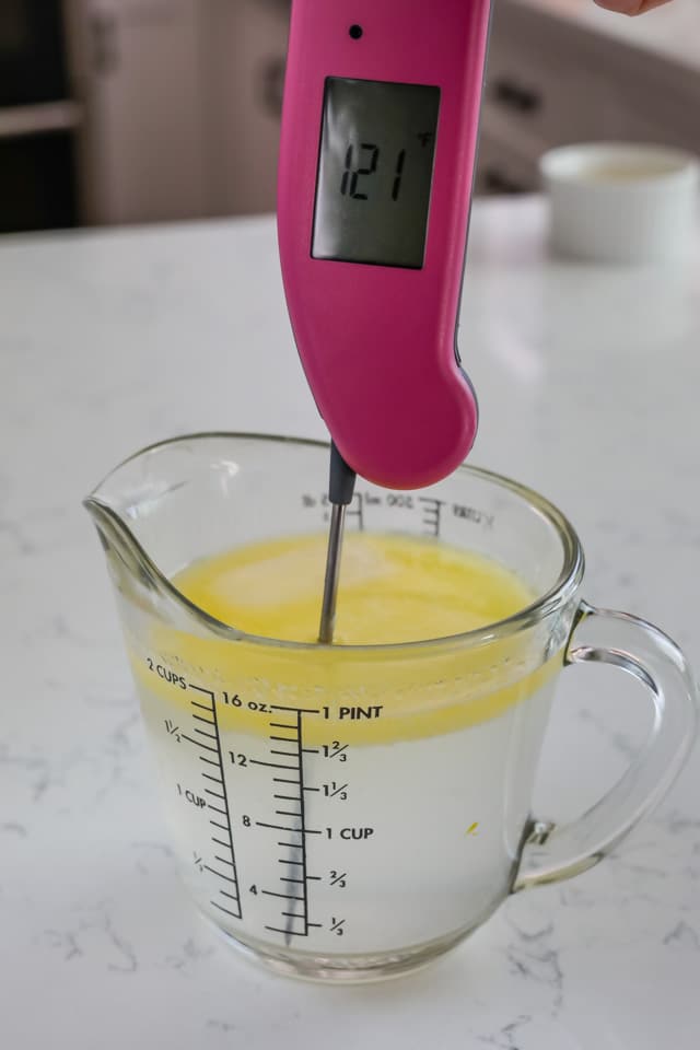 Melted butter in a liquid measuring cup with a pink thermometer taking the temperature