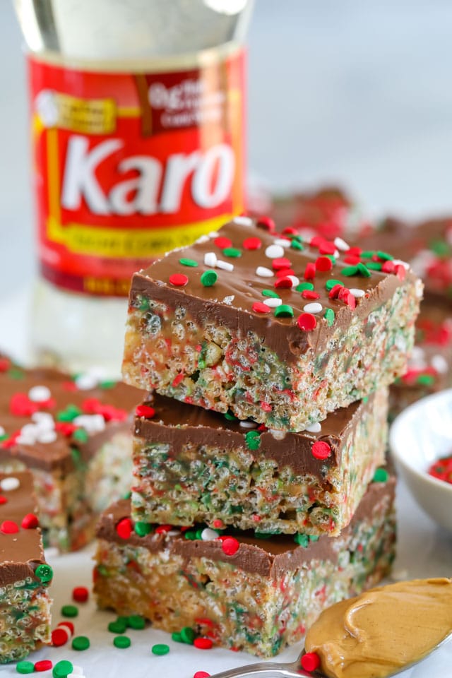 Three holiday no bake cereal bars stacked on top of eachother with corn syrup bottle in background