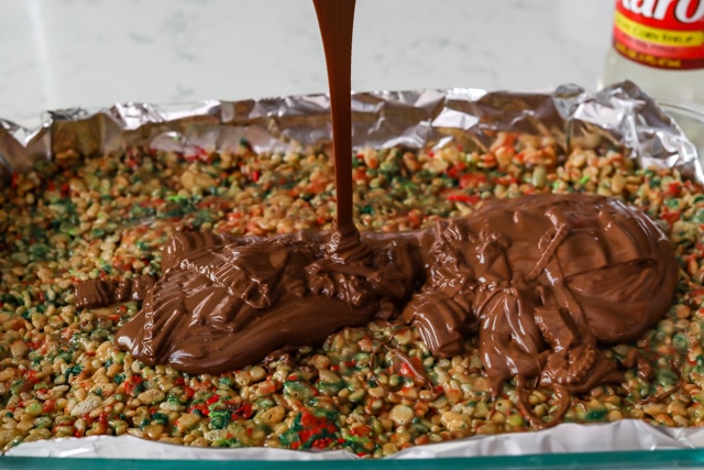 Melted chocolate being poured over cereal bars in a baking dish