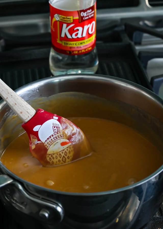 Corn syrup and peanut butter mixed together in pot on stove with red holiday spatula