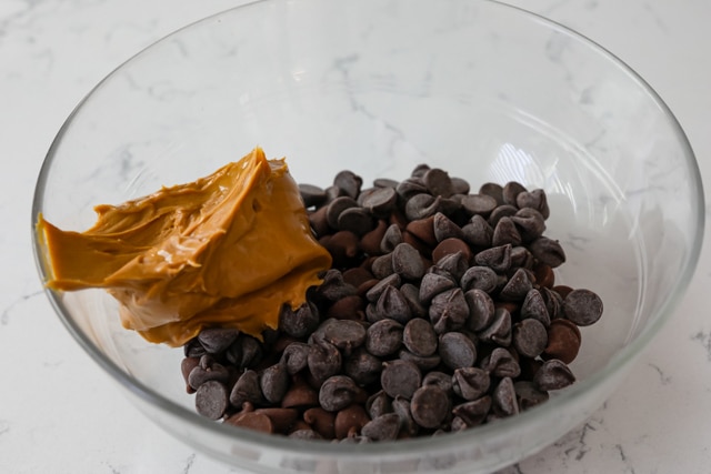 Chocolate chips and a scoop of peanut butter in a glass mixing bowl