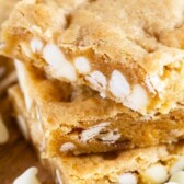 Stack of white chocolate blondies on a cutting board with white chocolate chips scattered around with recipe title on top