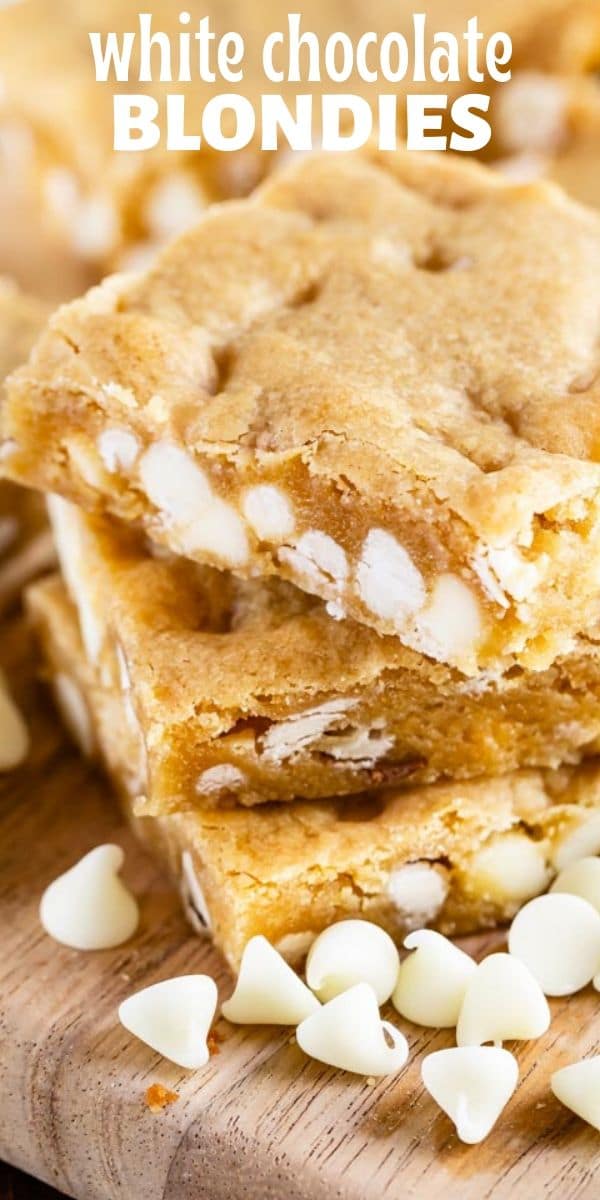 Stack of white chocolate blondies on a cutting board with white chocolate chips scattered around with recipe title on top