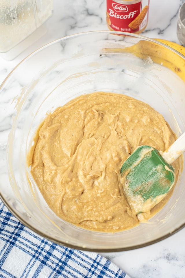 Biscoff banana bread batter in a clear mixing bowl with green spatula